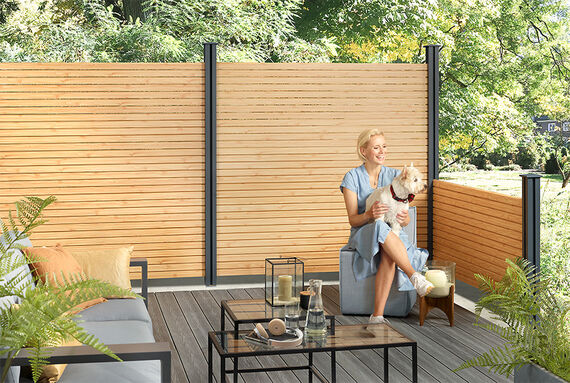 Woman pets her dog on a garden deck surrounded by Osmo Alu-Fence Rhombus in larch.