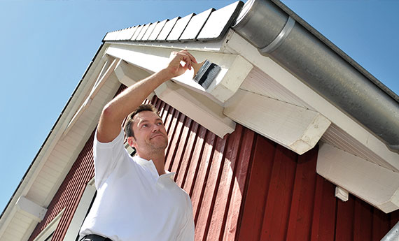 Mann streicht den Dachüberstand mit dem Pinsel und weißer Osmo Farbe OSMO