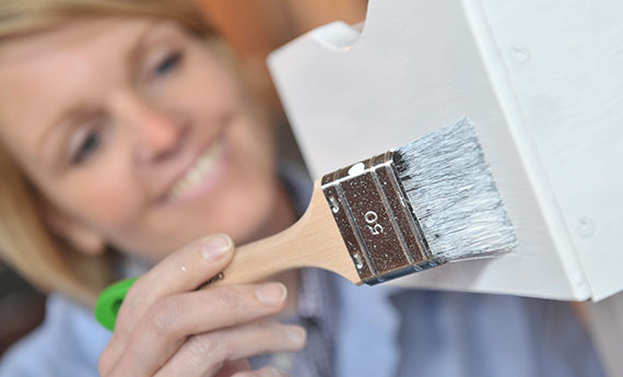 [Translate to EN:] Osmo Farbe und Anstriche - Frau streicht Holzmöbel an OSMO