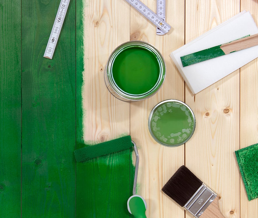 Wooden planks partially coated with Osmo wood stain in green and a selection of Osmo tools
